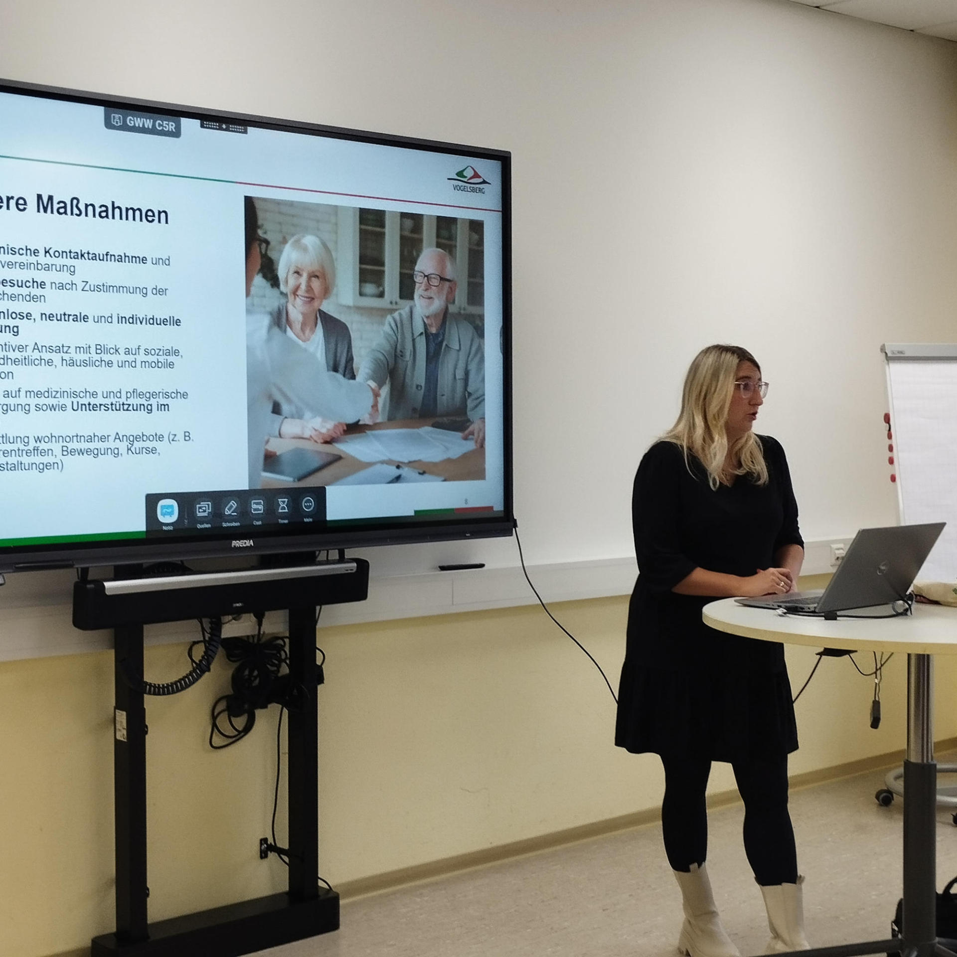 Eine Frau präsentiert an einem Display die Aufgaben einer Beratungsstelle für Senioren.