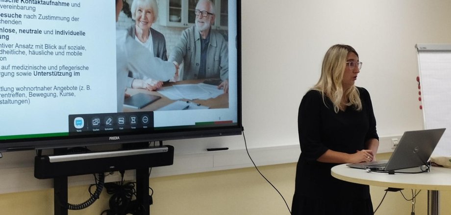 Eine Frau präsentiert an einem Display die Aufgaben einer Beratungsstelle für Senioren.