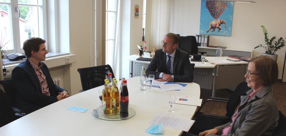 Florian Rausch, der Erste Kreisbeigeordnete Dr. Mischak und Angelika Boese beim Gespräch im Dienstzimmer. Sie sitzen an einem großen weißen Tisch