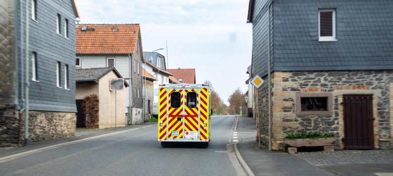 Ein Rettungswagen fährt auf einer Straße, die durch einen Ort führt. Rechts und links stehen Häuser