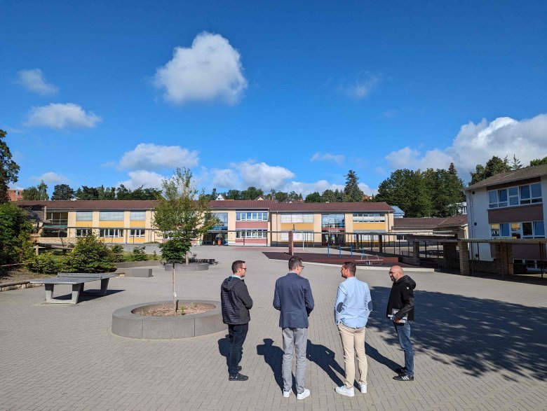 Viel Platz, Spiel-, Sitz- und Sportmöglichkeiten stehen am relativ frisch sanierten Schulhof der GHS zur Verfügung. Vier Männer stehen mit dem Rücken zur Kamera und schauen auf einen weiträumigen Schulhof