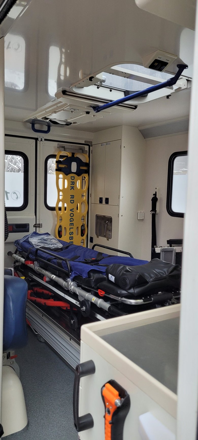 Innenaufnahme eines Rettungswagens. darauf ist unter anderem eine blaue und eine gelbe Trage zu sehen. Außerdem sieht man geschlossene Einbauschränke