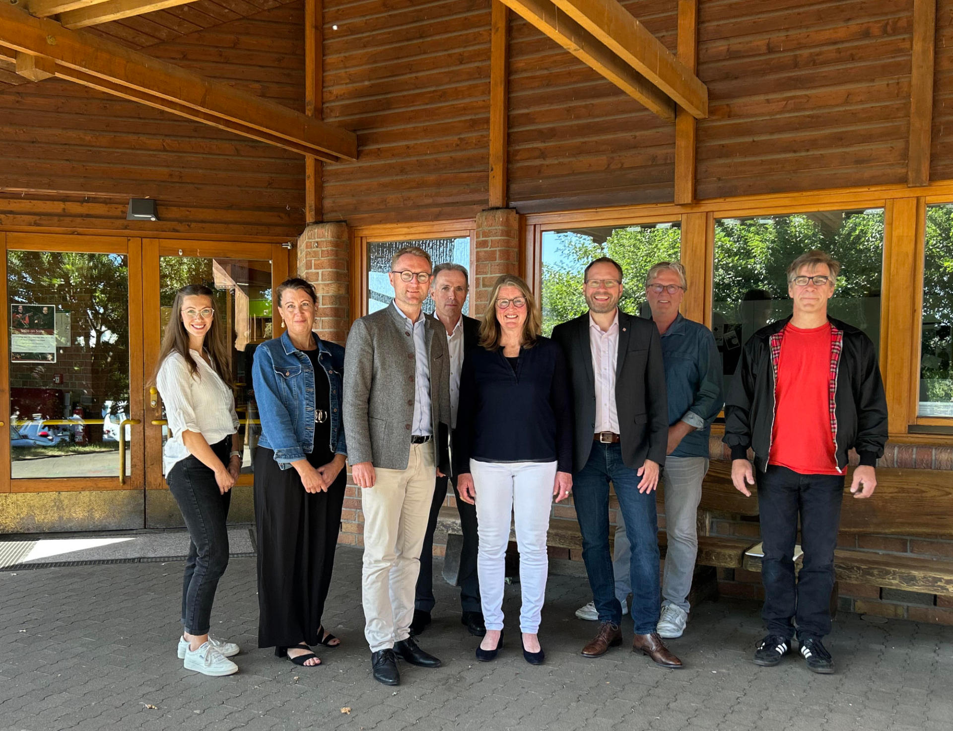 Acht Menschen haben sich im Eingangsbereich einer SChule zum Gruppenbild aufgestellt. Sie lächeln in die KAmera. 