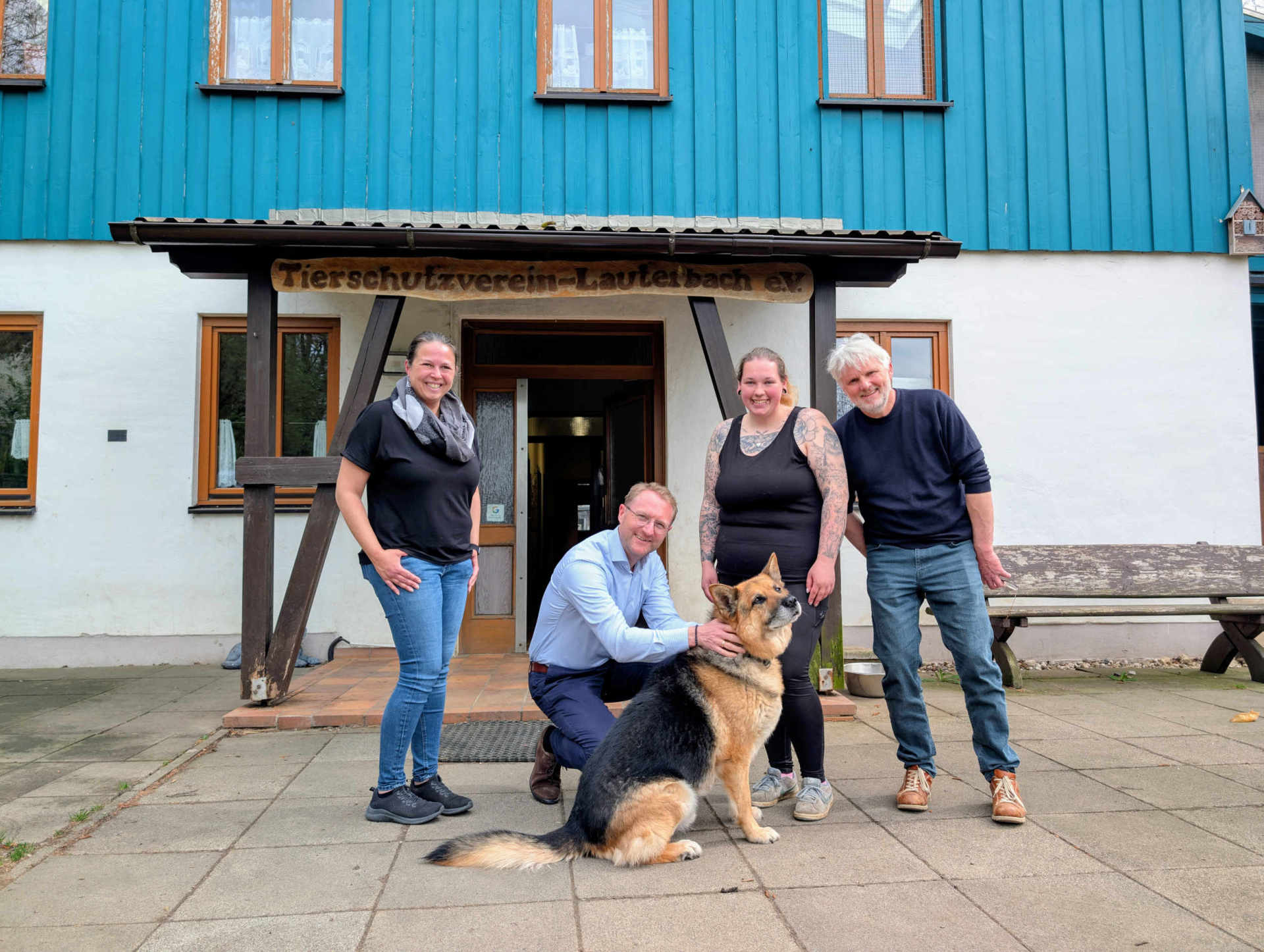 Vier Menschen haben sich vor einem Tierheimeingang zum Gruppenfoto aufgestellt. Mit auf dem Bild ist auch ein Schäferhund. 