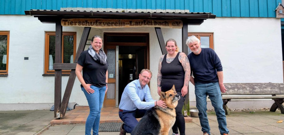 Vier Menschen haben sich vor einem Tierheimeingang zum Gruppenfoto aufgestellt. Mit auf dem Bild ist auch ein Schäferhund. 