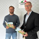 Zwei Männer stehen vor einer Wand und lächeln in die Kamera. Sie präsentieren ein Heft, das Kinder zur Bewegung animieren soll.