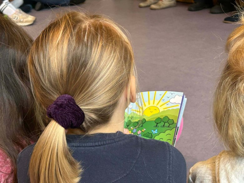Ein Mädchen im Grundschulalter liest in einem Kinderbuch. Sie ist nur von hinten zu sehen.