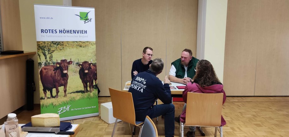 Vier Menschen sitzen an einem Tisch und tauschen sich zu direkt vermarkteten Lebensmitteln aus. 
