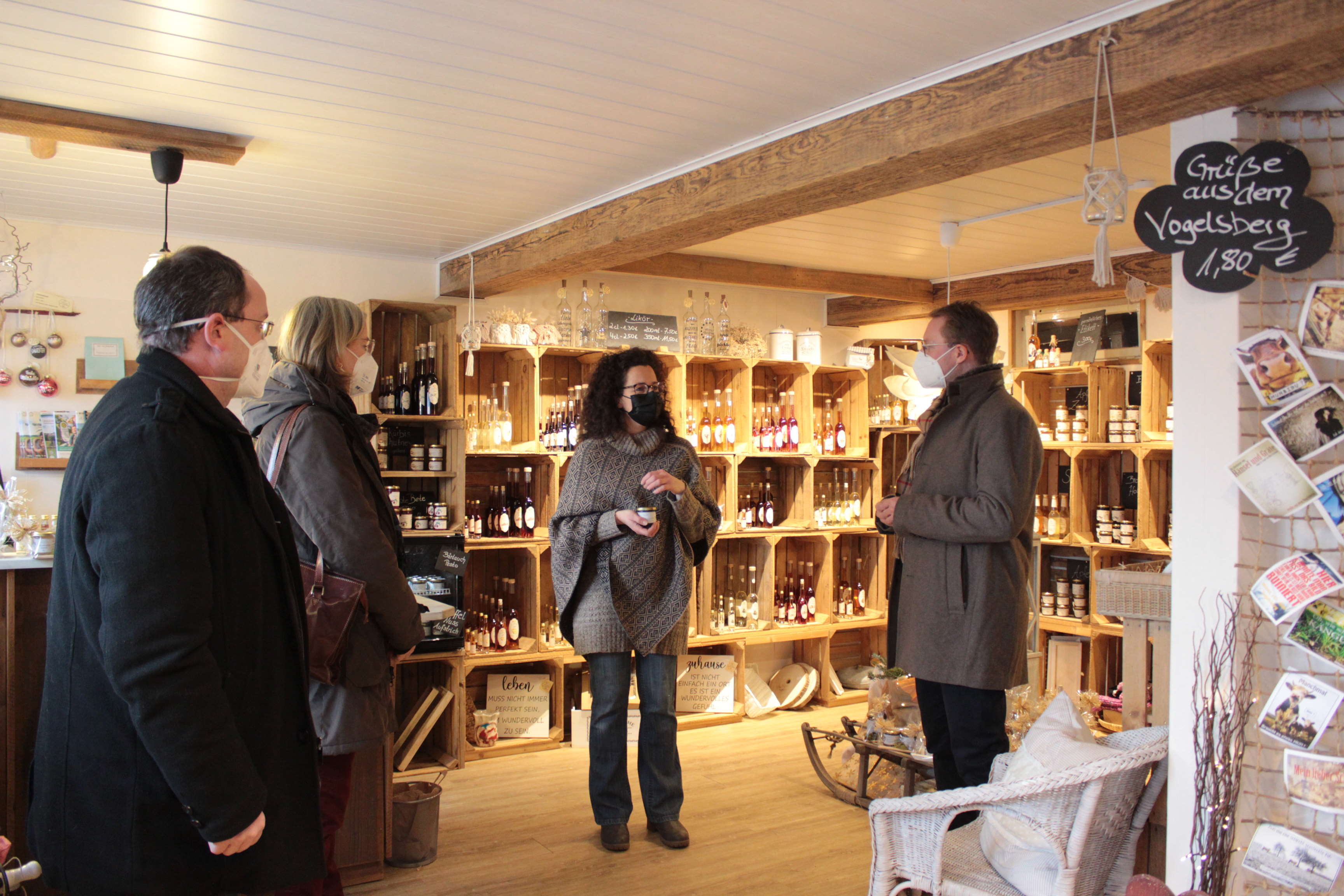 In ihrem kleinen LAden mit Likören und Fruchtaufstrichen erläutert Katja Wittmann (Mitte) ihr Konzept – Der Erste Kreisbeigeordnete Dr. Jens Mischak (von rechts) hört gemeinsam mit Andrea Ortstadt von der Wirtschaftsförderung des Vogelsbergkreises und Sebastian Stang, Bürgermeister der Gemeinde Grebenhain, gespannt zu. 