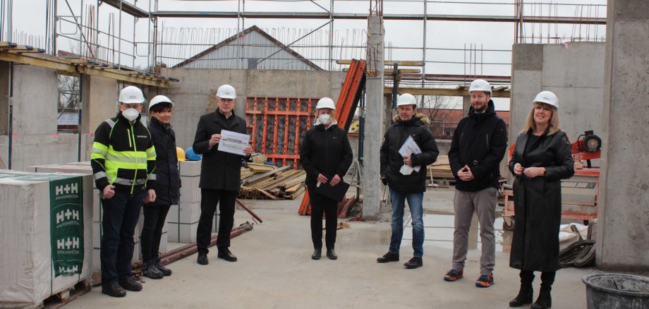 Auf einer Rohbaustelle. Viel Baumaterial ist im Hintergrund zu sehen. Landrat Manfred Görig (Dritter von links), macht sich gemeinsam mit Sebastian Stang (links), Bürgermeister der Gemeinde Grebenhain, Andrea Wolf (von rechts), Schulleiterin der Oberwaldschule Grebenhain, Sebastian Birx, Leiter der Jahrgangsstufen 5 bis 7, ein Bild vom Baufortschritt an der OWS. Architekt Matthias Losacker, Christine Jüngst, örtliche Bauleitung der Architekten Ritz & Losacker GmbH, und Claudia Wauschkuhn vom AHEG erläutern die aktuellen Schritte und Besonderheiten.