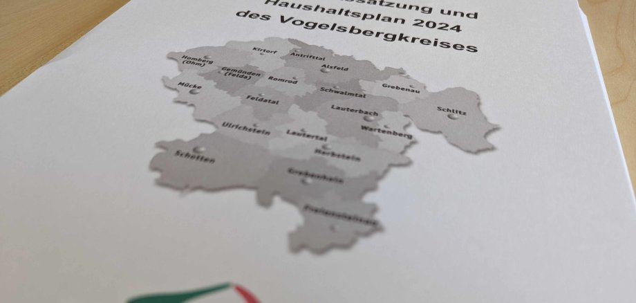Aufnahme des Deckblatts des Kreishaushaltes 2024. Darauf zu erkennen eine Karte des Vogelsbergkreises und das Logo. Ein stilisierter Vulkan mit schwarzen, roten und grünen Linien