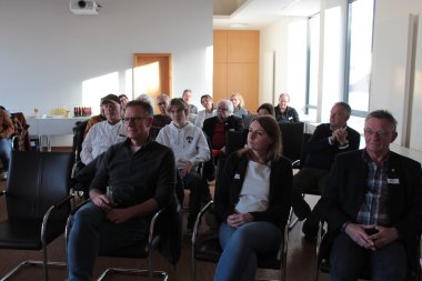 Zahlreiche Menschen sitzen in einem Sitzungssaal in Stuhlreihen