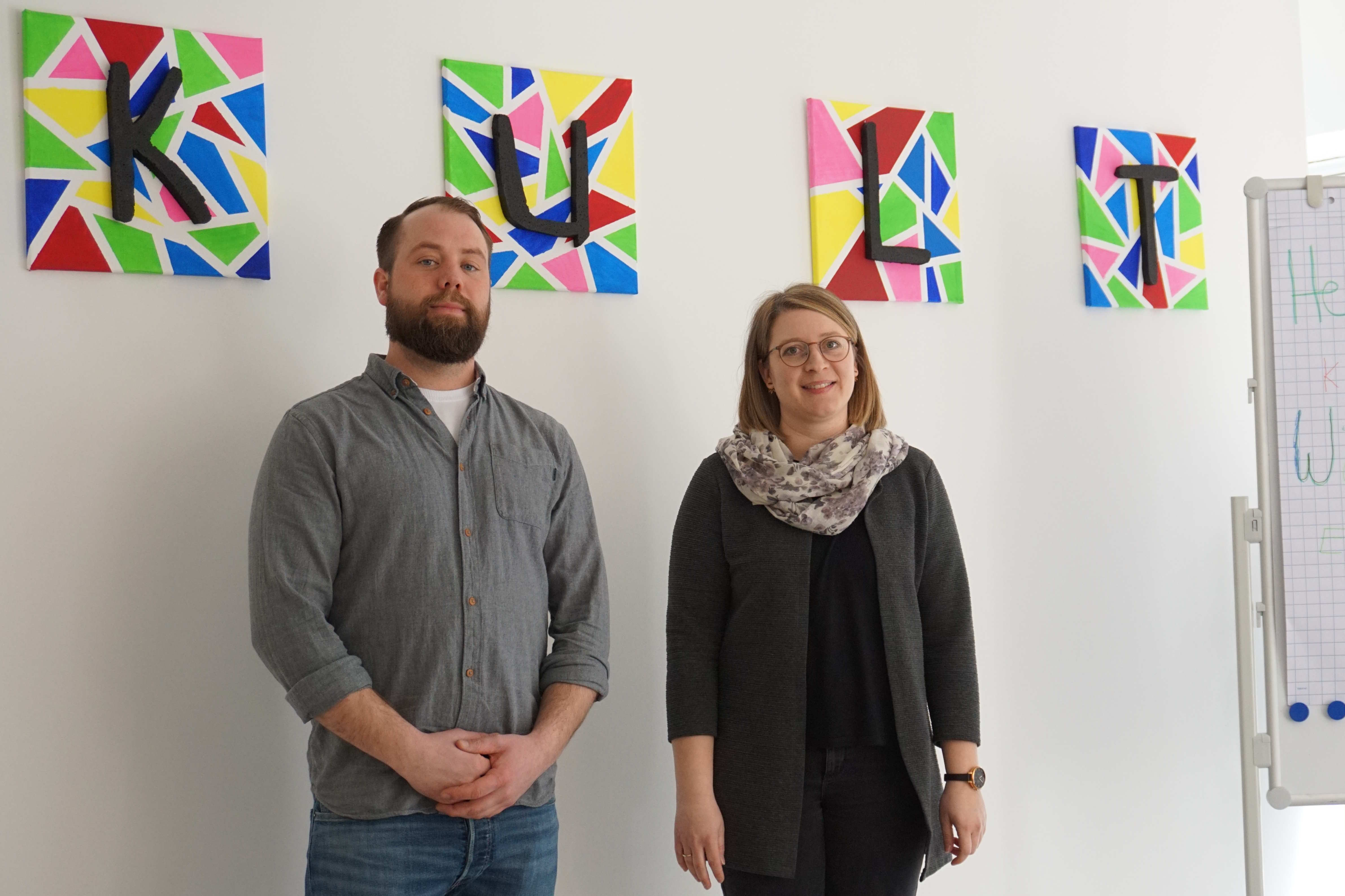„Wir sind K.U.L.T.“: Die Sozialarbeiter Daniela Christ und Simon Thiel bilden das „K.U.L.T.“-Team. Sie haben sich niedrigschwellige Beratung in vielen Lebenslagen auf die Fahnen geschrieben. Sie stehen vor einer weißen Wand. 