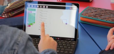 Ein Drittklässler bedient ein Tablet. Darauf sind erste Programmierübungen zu sehen. 