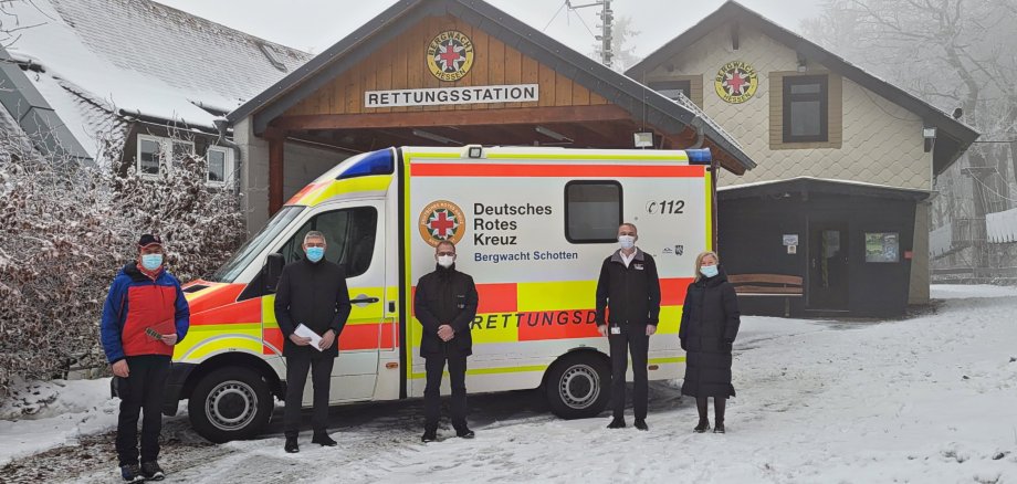 Fünf PEersonen stehen vor der Bergwacht in Schotten. Davor ist außerdem ein Rettungswagen geparkt. Es liegt Schnee und Nebel in der Luft. 