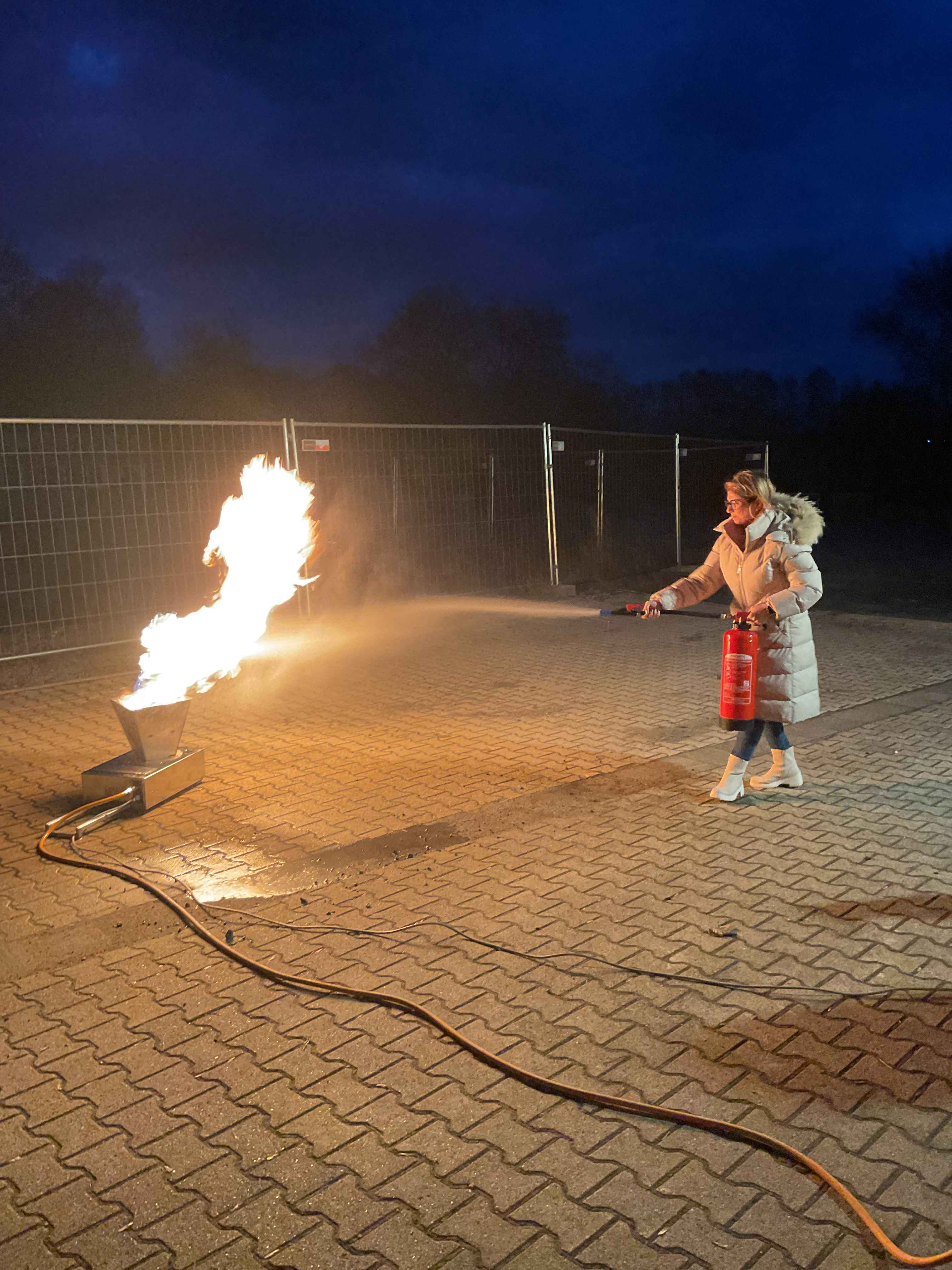 Selbst ausprobiert: Beim Besuch der Feuerwehr löschen die Dolmetscher einen Brand mithilfe eines Feuerlöschers. Eine Frau sprüht mit einem ÜBungsfeuerlöscher auf eine Gasflamme.
