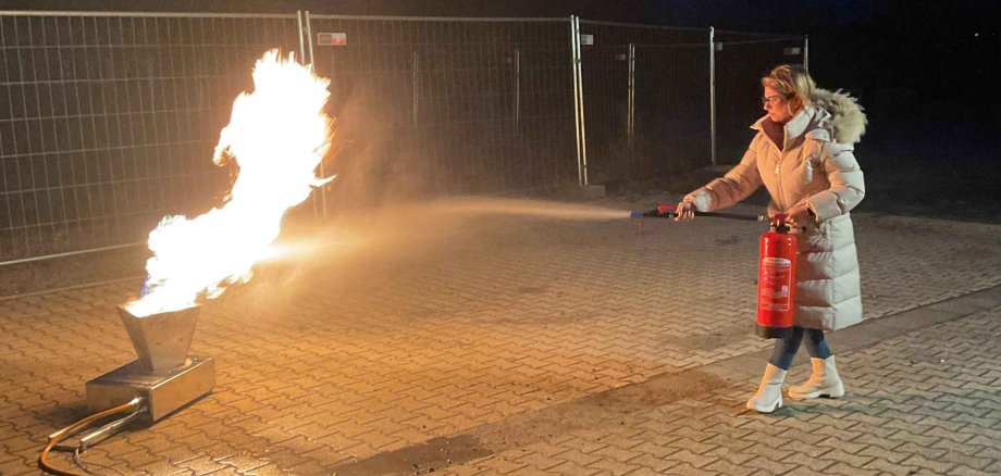 Selbst ausprobiert: Beim Besuch der Feuerwehr löschen die Dolmetscher einen Brand mithilfe eines Feuerlöschers. Eine Frau sprüht mit einem ÜBungsfeuerlöscher auf eine Gasflamme.
