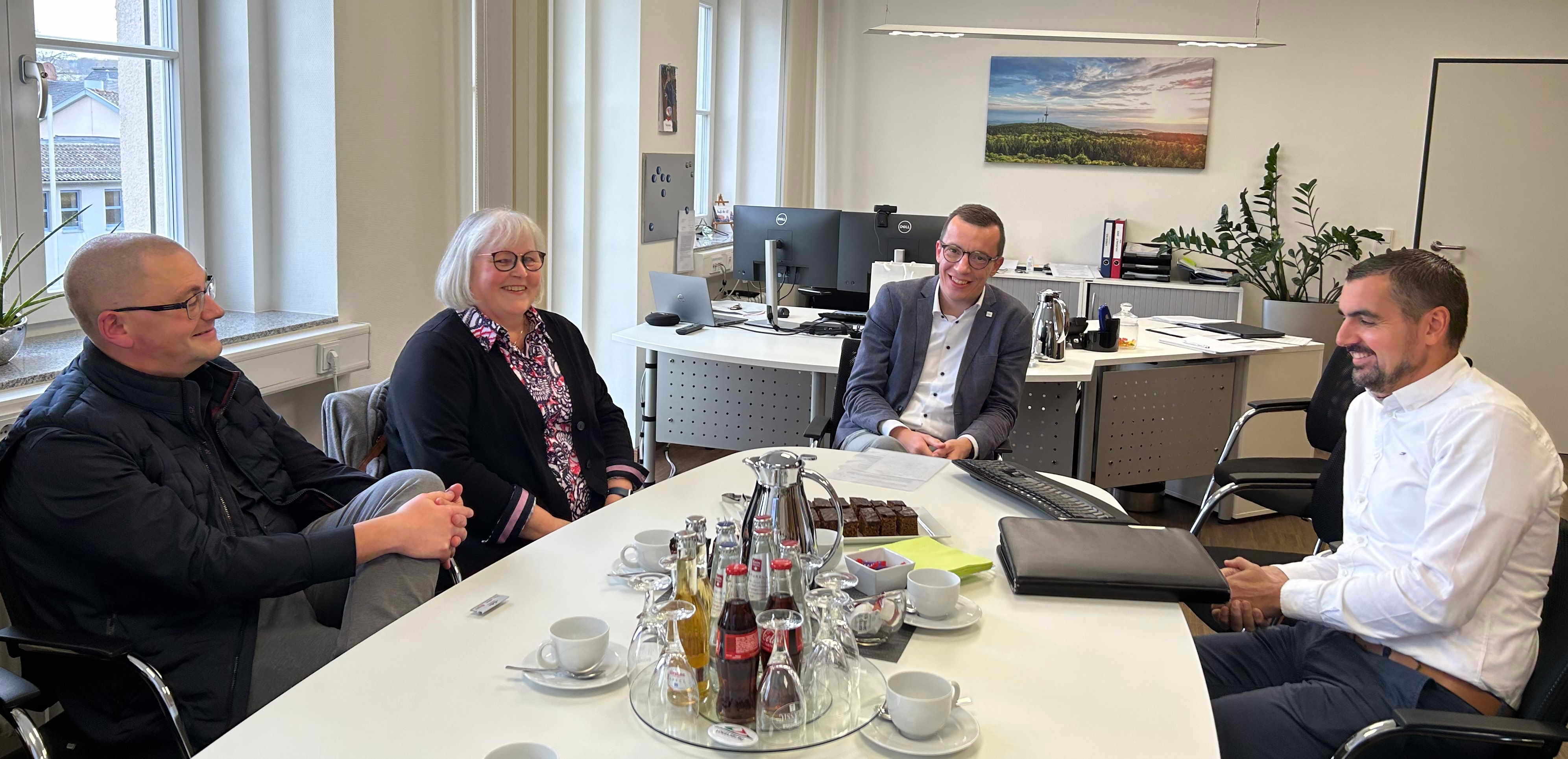 Vier Menschen sitzen an einem Konferenztisch. Sie unterhalten sich locker und lächeln. 