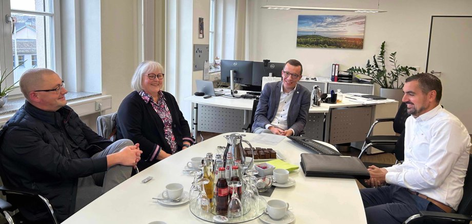 Vier Menschen sitzen an einem Konferenztisch. Sie unterhalten sich locker und lächeln. 
