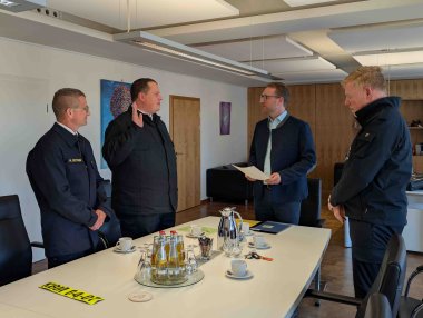 Vier Männer stehen um einen Konferenztisch herum. Sie haben sich für eine Vereidigung erhoben. Ein Mann in Feuerwehruniform hat die rechte Hand zum Eid erhoben.