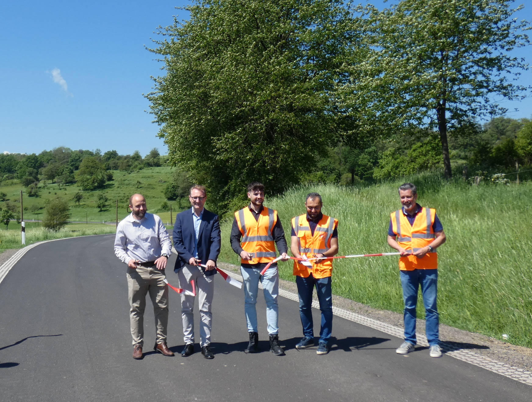 Fünf Männer stehen auf einer erneuerten Straße und schneiden ein Band durch. Sie geben die Straße symbolisch für den Verkehr frei.