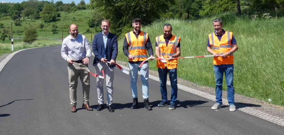 Fünf Männer stehen auf einer erneuerten Straße und schneiden ein Band durch. Sie geben die Straße symbolisch für den Verkehr frei.