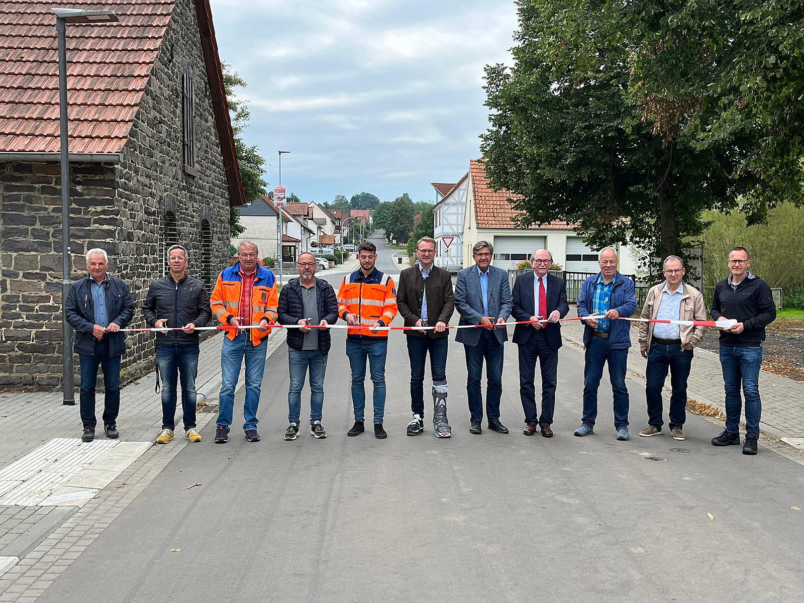 Verkehrsfreigabe in Frischborn. Elf Männer stehen auf der Straße und durchschneiden symbolisch ein Band.