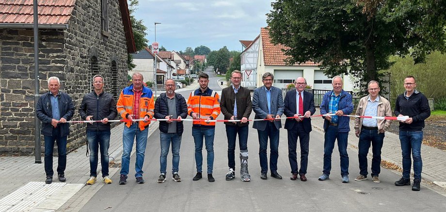 Verkehrsfreigabe in Frischborn. Elf Männer stehen auf der Straße und durchschneiden symbolisch ein Band.