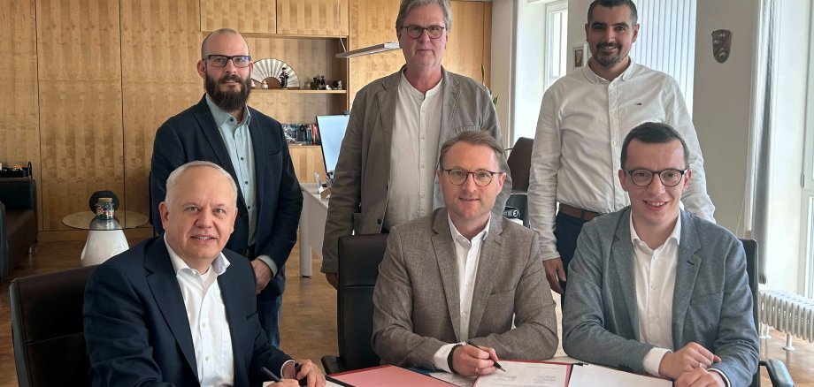Sechs Männer sind für ein Gruppenbild zusammengekommen. Sie unterzeichnen einen Kooperationsvertrag