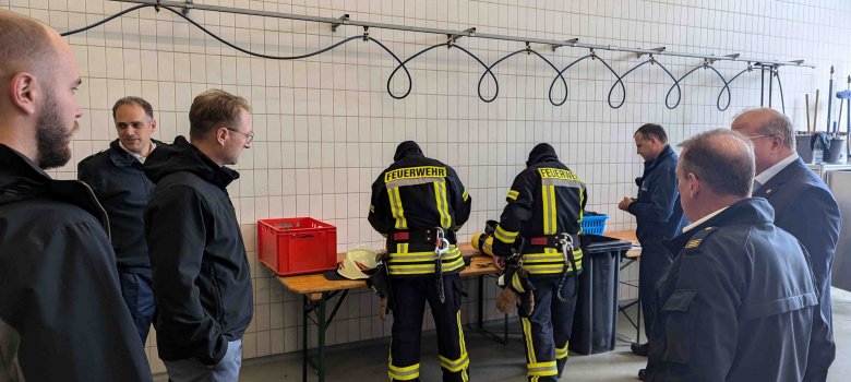 Zwei Feuerwehrleute bereiten sich auf eine Übung vor. Mehrere Menschen verfolgen die Vorbereitungen interessiert.